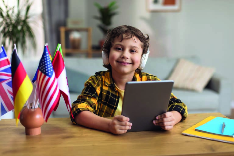 Garoto estudando com fones de ouvido
e com um tablet nas mãos. Educação bilíngue e internacional, quais as diferenças?