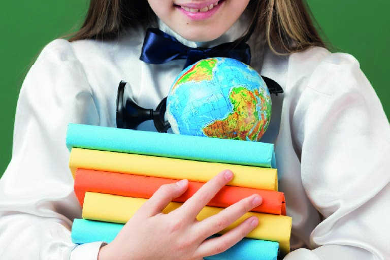 Aluna segurando livros e em cima deles um globo terrestre. Educação bilíngue e internacional, quais as diferenças?