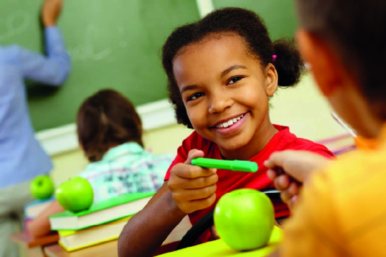 Imagem - criança em sala de aula passando uma canetinha para o colega. Como acolher novos alunos em uma escola bilíngue?